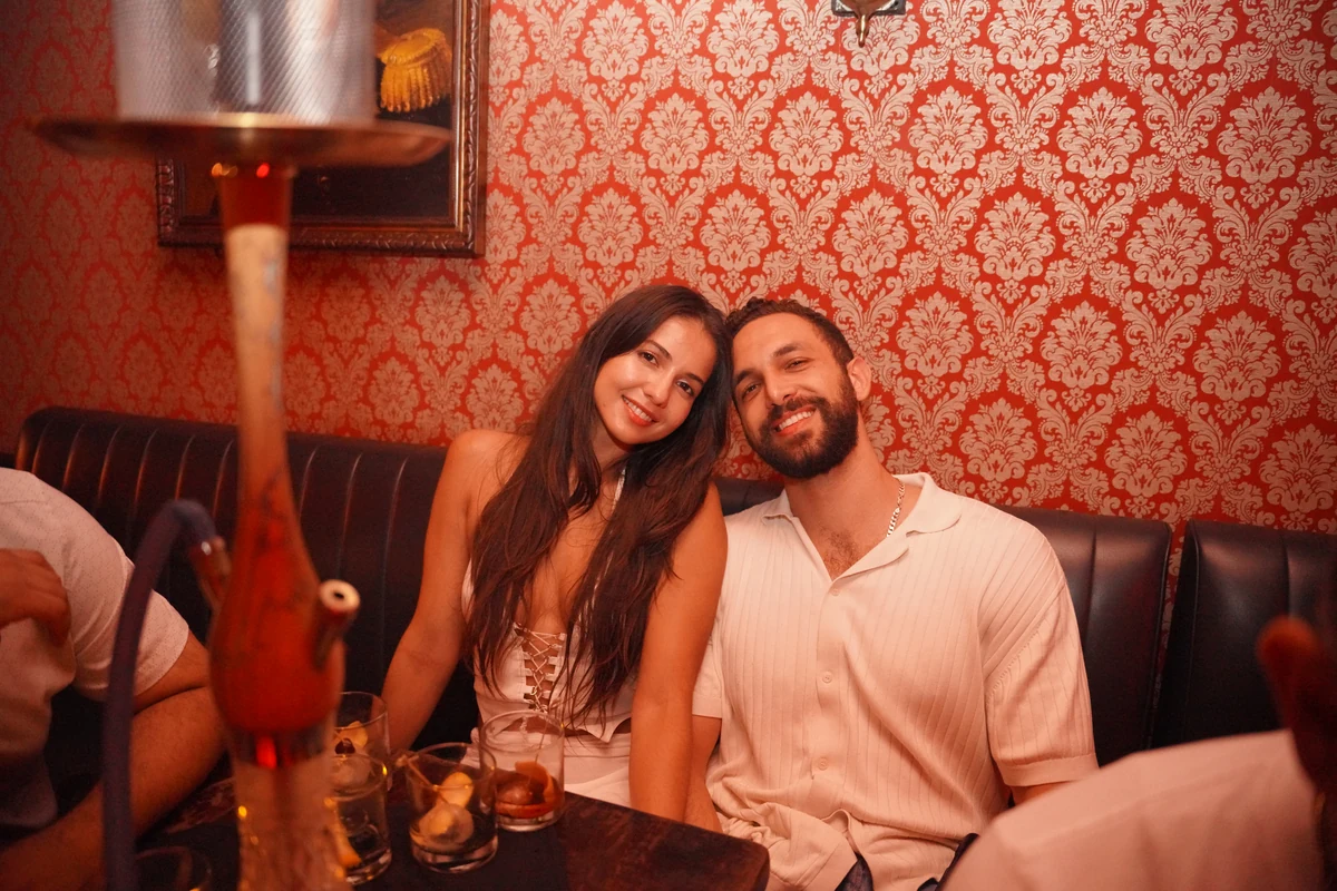A smiling couple seated close together against red patterned wallpaper